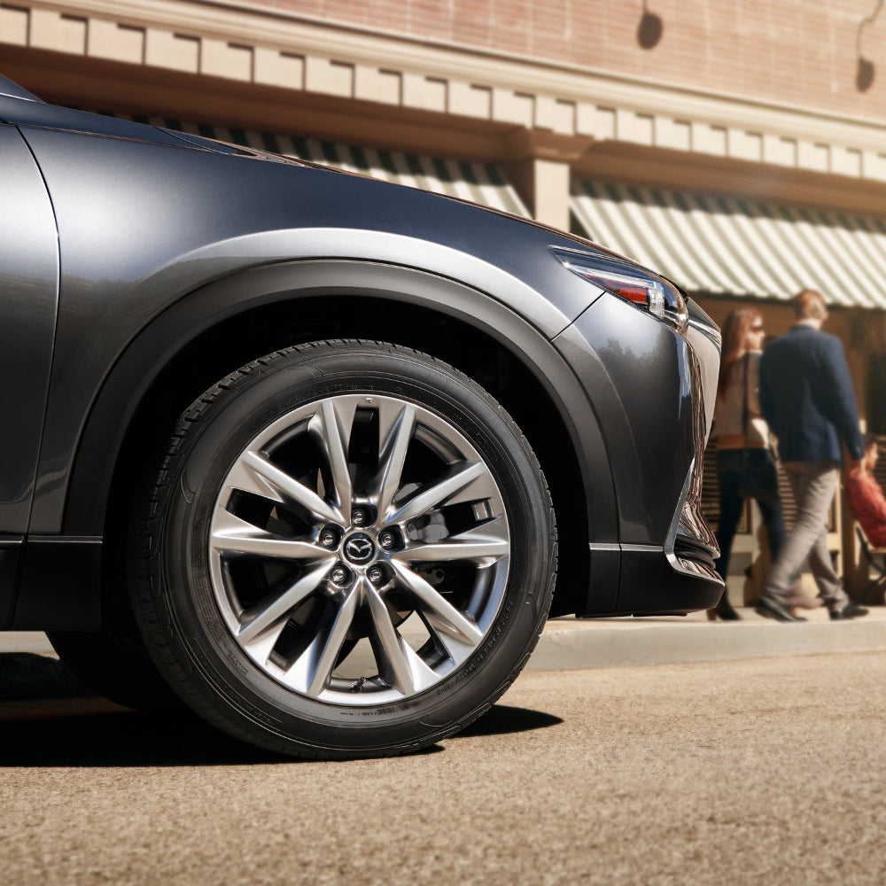 Close-up of a car wheel with a blurred background of people and a building.