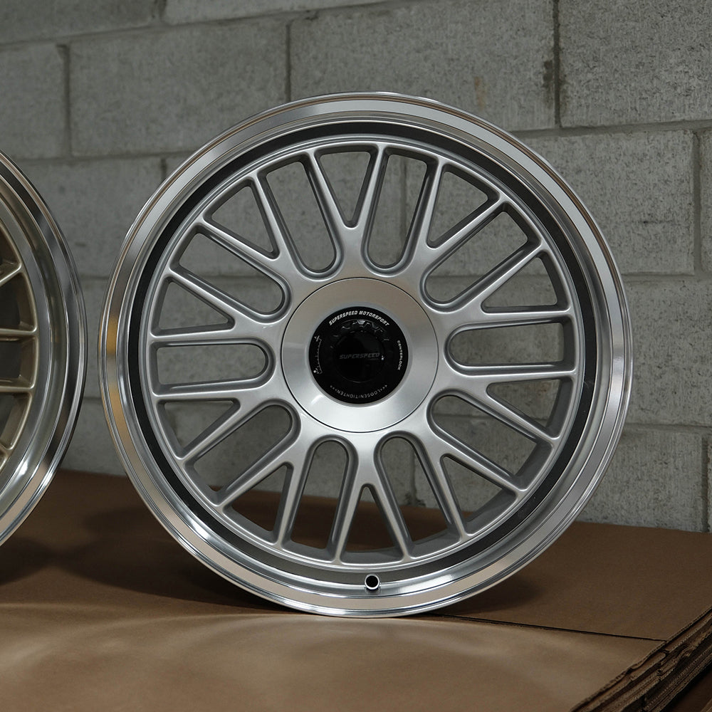 Close-up of a silver alloy wheel on a cardboard box with a gray brick wall background